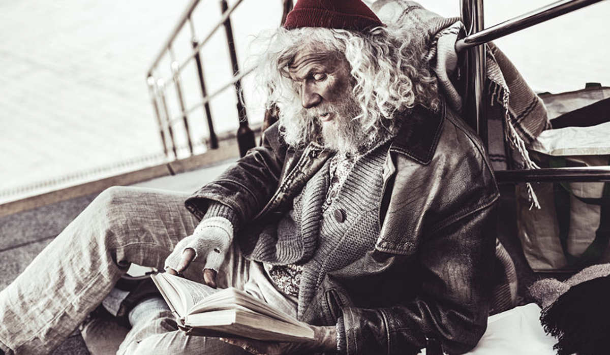 Old dirty loafer reading book that passer by giving him