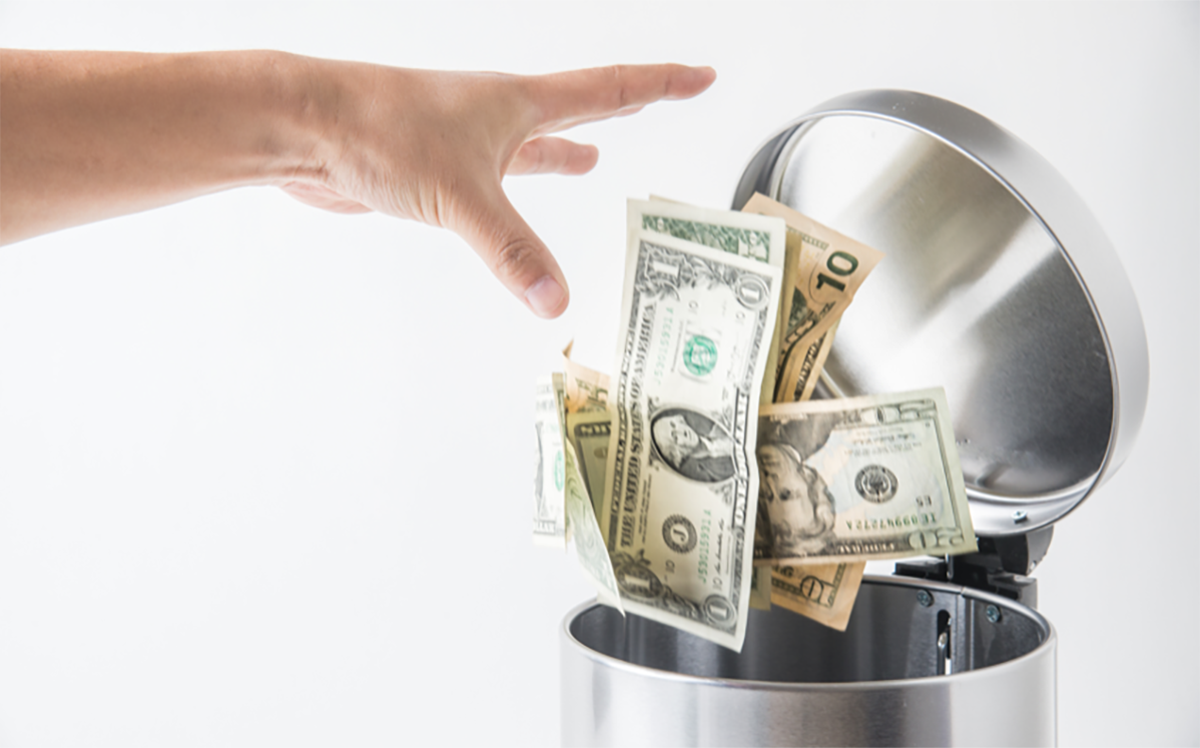 A person throwing money into the trash bin