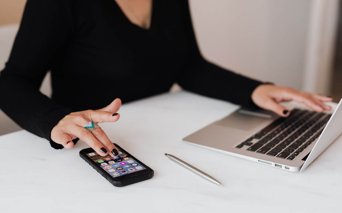 A woman using a password manager on her laptop and verifying MFA on her phone.