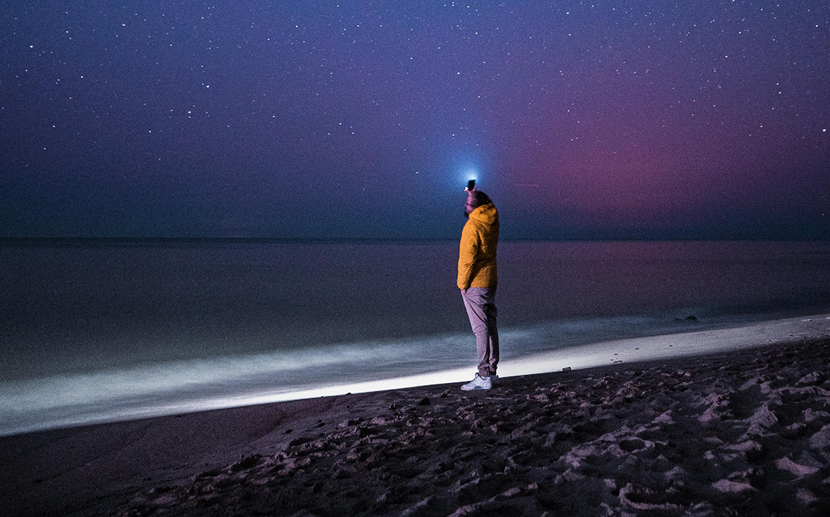 A person alone on a beach at night, holding up a light under a starry sky—symbolizing the importance of preparing and guiding your legacy through thoughtful beneficiary planning