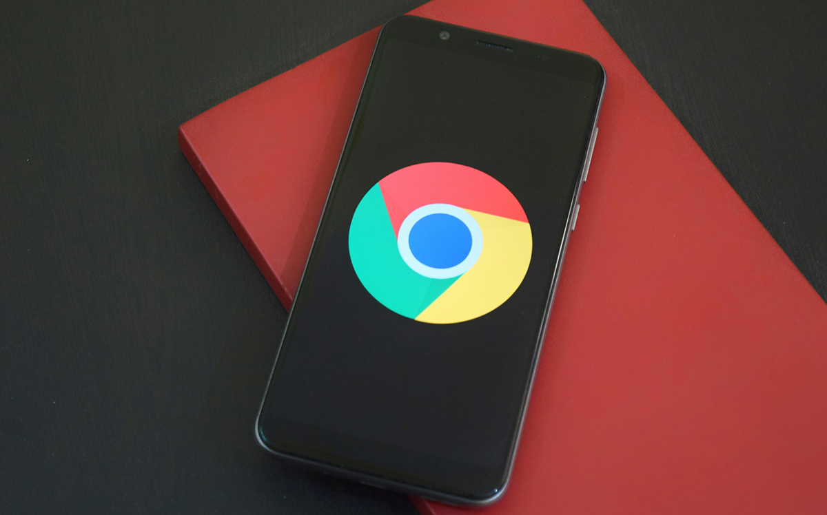 A smartphone displaying the Google Chrome logo on its screen, placed on top of a red notebook on a dark desk — symbolizing the critical Chrome security vulnerability recently patched.