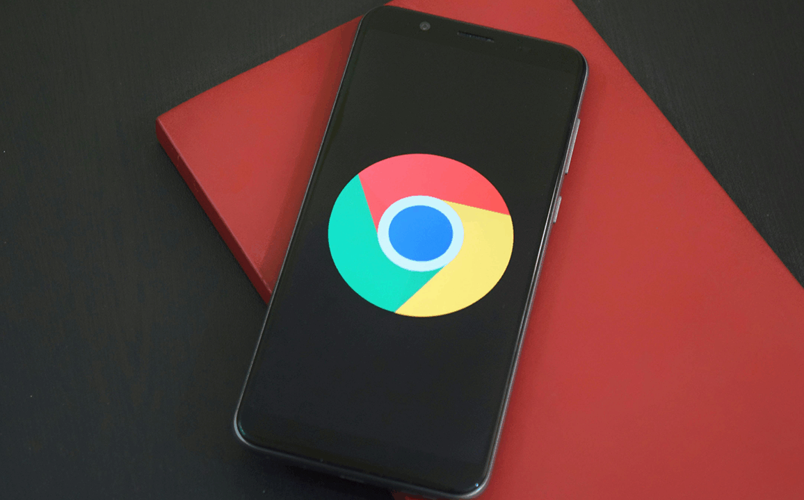 A smartphone displaying the Google Chrome logo on its screen, placed on top of a red notebook on a dark desk — symbolizing the critical Chrome security vulnerability recently patched.